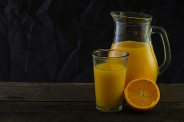 Jug and glass with fresh orange juice, still life art on dark ba