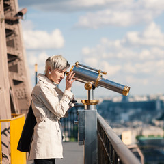 Young blonde woman looks through telescope on top of the Eiffel