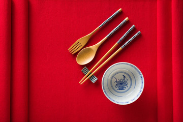 Chinese bowl, fork, spoon and chopsticks on red mat top view