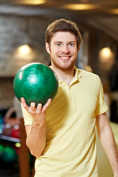 happy young man holding ball in bowling club