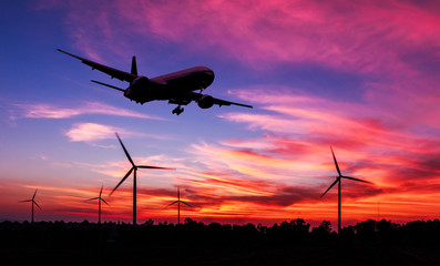 silhouette air plane flying on wind turbine farm at dusk