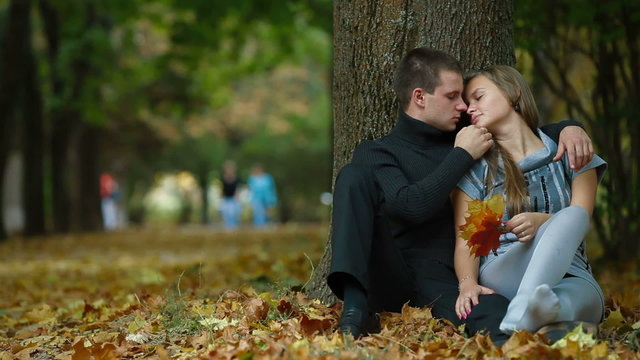 Young couple kissing on fallen leaves in autumn park
