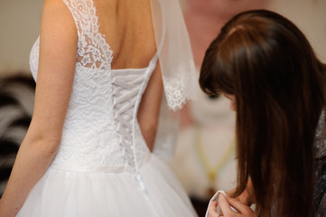 Obraz na płótnie Canvas bridesmaid helps the bride lace corset wedding dress