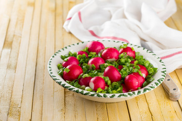 Bowl of red radishes and green onions on a wooden background