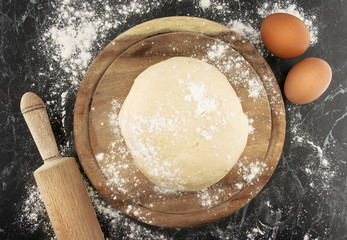 Dough on a wooden board. Rolling pin and egg on table. Top view