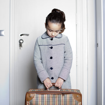 Ni&ntilde;a triste con maleta en la puerta de casa