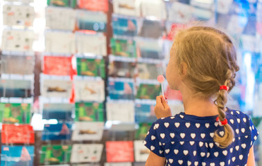 Little girl with lollipop near postcard kiosk.