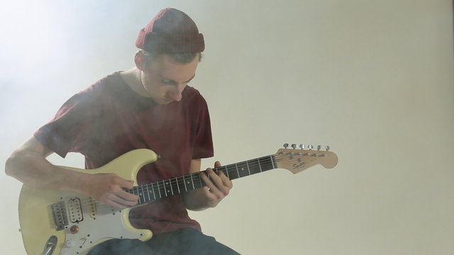 Guy in hat playing guitar in the studio in smoke