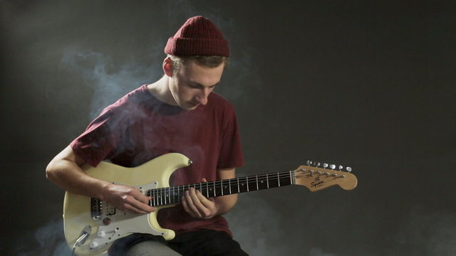 Thoughtful guitarist playing guitar in dark studio