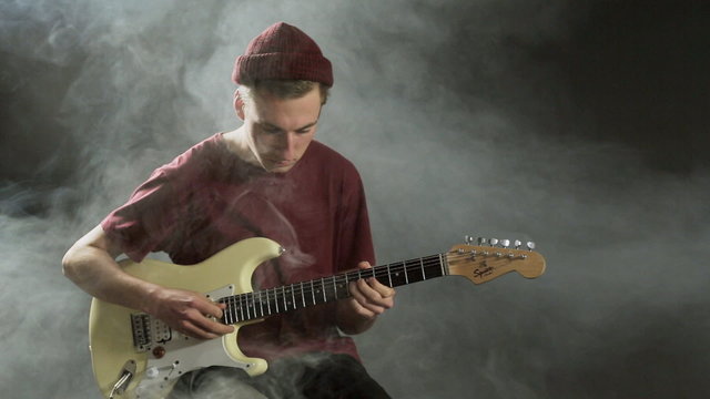 Young guy playing guitar in a dark studio in smoke