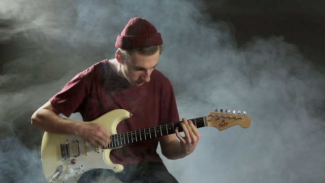 Young guy playing guitar in a dark studio in smoke