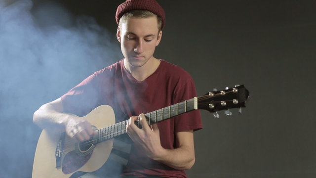 Talented young musician playing guitar in a dark studio in smoke