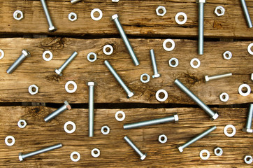 Fixing elements (nuts, washers, screws) on wooden background.