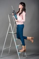 Attractive woman on ladder with heavy drill