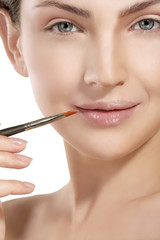 Beautiful model applying lip gloss with a brush