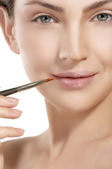Fototapeta premium Beautiful model applying lip gloss with a brush
