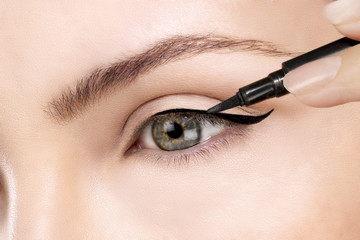 Beautiful model applying eyeliner closeup on eye - obrazy, fototapety, plakaty