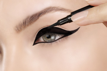 Beautiful model applying eyeliner closeup on eye