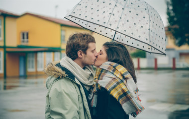 Young couple kissing outdoors under umbrella in a rainy day