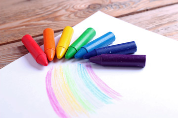 Oil pastel crayons lying on a paper with painted rainbow