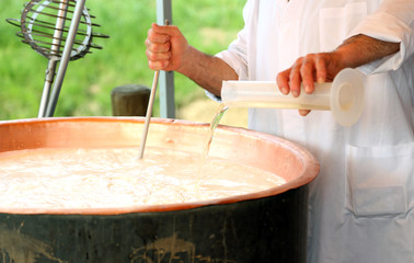 old Cheesemaker pours milk rennet in copper pot for making chees