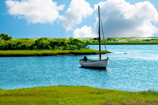 Sailboat anchored in a blue pond or lake, with green grass banks