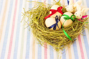 Obraz premium Easter eggs and two rabbits in nest on stripe textile background