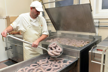 Man taking cooked sausages from cauldron in a butchery