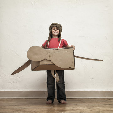 Proud little boy playing with pilot hat and cardboard box airplane