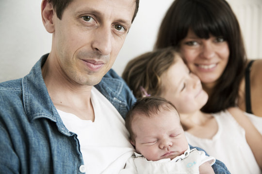 Young parents with male newborn and little daughter sitting on sofa at home