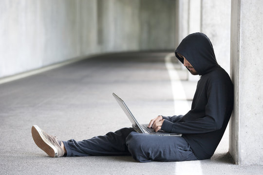 Hacker with laptop sitting in an underground car park