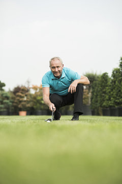 Golf player crouching on turf looking at golf ball