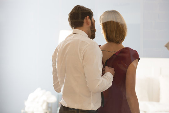 Man unzipping woman's dress in bedroom