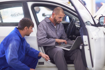 Two car mechanics with laptop in repair garage