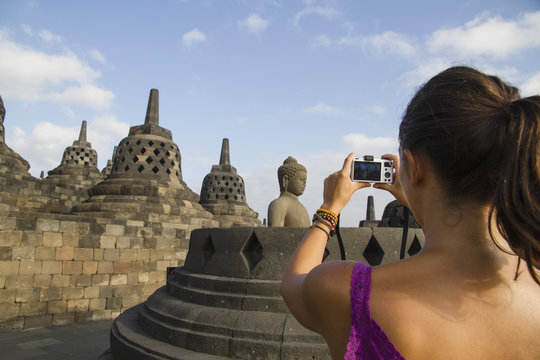 Indonesia, Young woman taking photo of Buddha statue at Borobudur Temple