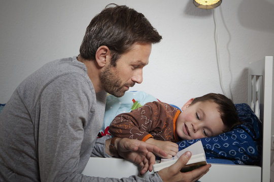 Germany, Berlin, Father reading book while son sleeping