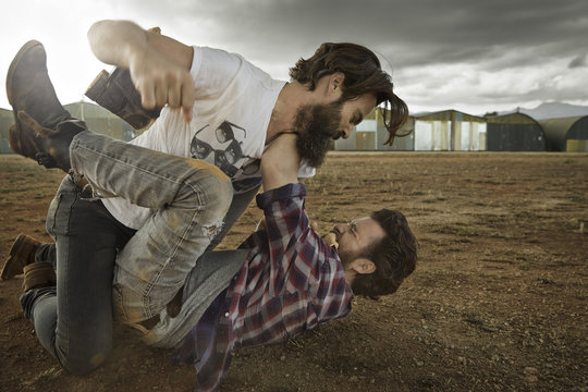 Two men with full beards fighting in abandoned landscape