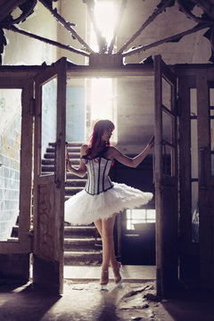 Germany, Brandenburg, Beelitz, woman with red hair and ballerina dress standing in destroyed old house at backlight