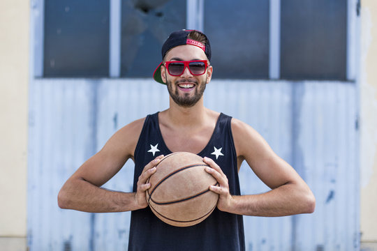 Portrait of smiling young man with basketball wearing baseball cap and sunglasses