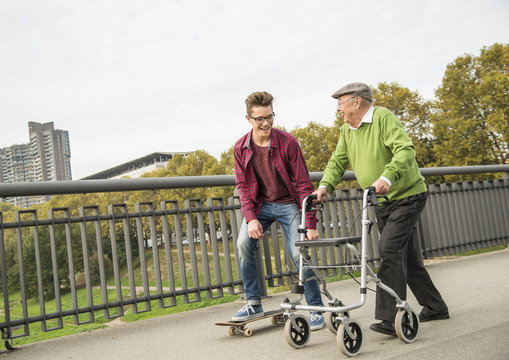 Happy senior man with wheeled walker and adult grandson with skateboard
