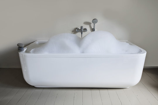 Bathtub with soapsuds and pebbles in bathroom