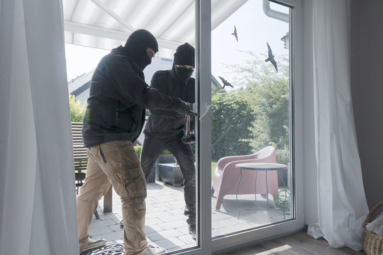 Two burglars opening terrace door of an one-family house with hammer and crowbar at daytime