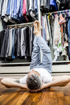 Man with hands behind his head and feet up in the air lying on the floor of his walk-in closet