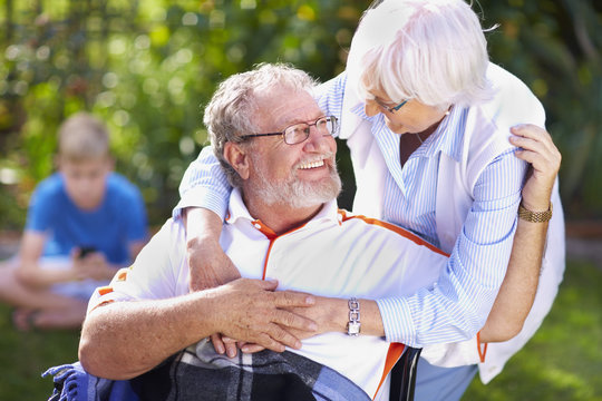 Senior woman embracing husband in wheelchair