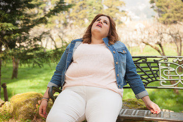 Fatigued woman with overweight sitting in a park bench.