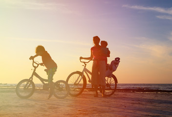 happy mother with kids biking at sunset
