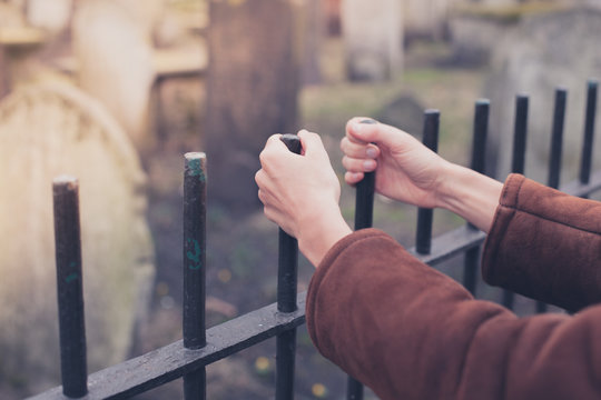 Hands holding fence at graveyard