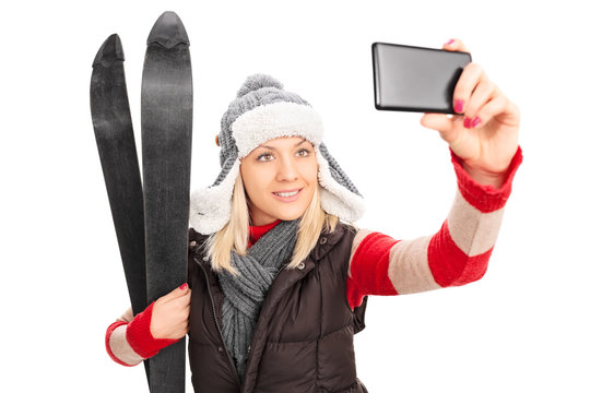Woman holding a pair of skis and taking selfie