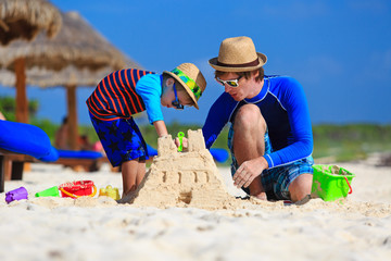 father and son building sand castle on tropical beach