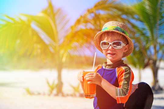 cute little boy drinking juice on tropical beach